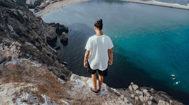 Man standing on a cliff and looking at water