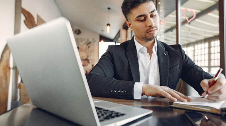Student in suit writing in front of laptop