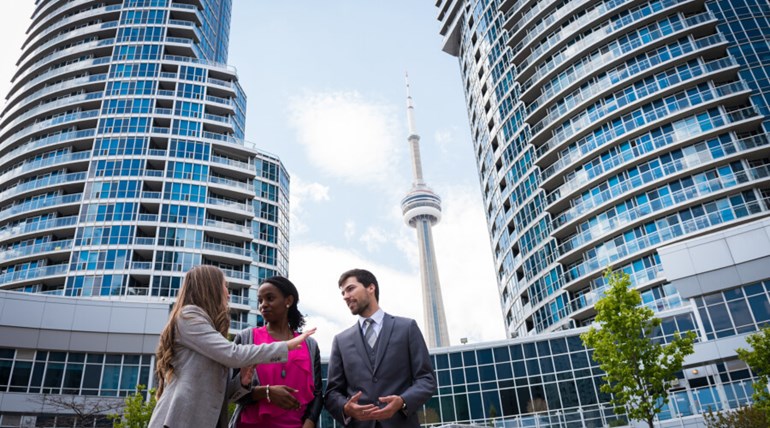 Three people talking in front on buildings and CN Tower