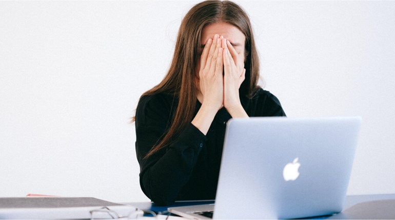 Woman with her face in her hands in front of laptop