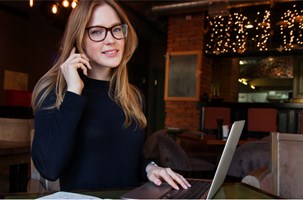 Woman with glasses talking on phone in front of laptop