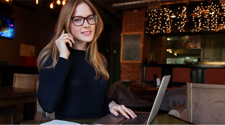 Woman with glasses talking on phone in front of laptop