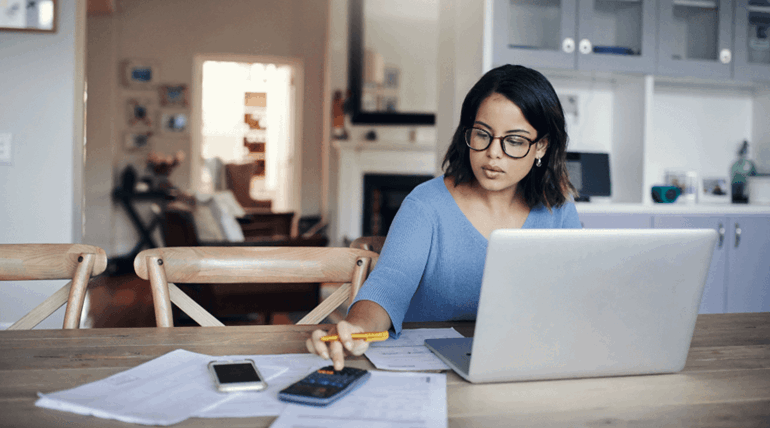 Woman using a calculator in front of laptop