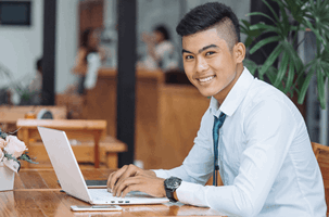Young student smiling at the camera while facing a laptop