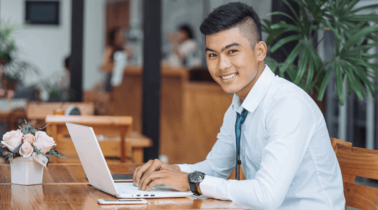 Young student smiling at the camera while facing a laptop