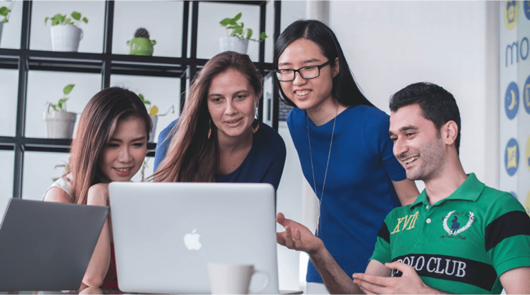 A group of students talking while using a laptop