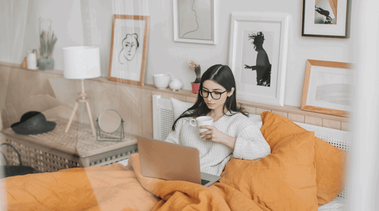 Woman holding cup and using laptop