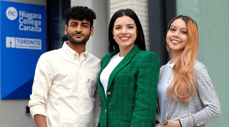 A group of three smiling people standing outside the college