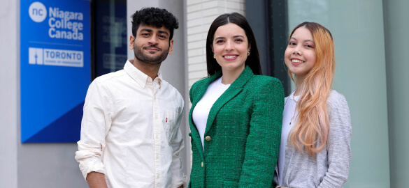A group of three smiling people standing outside the college