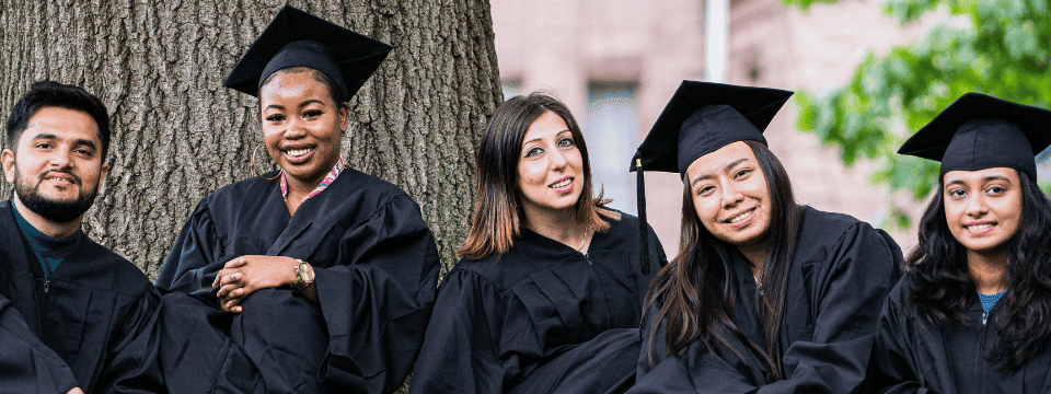 Graduates in gowns posing outdoors by a tree