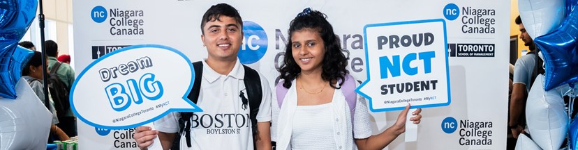 Two students holding “Dream Big” and “Proud NCT Student” signs at Niagara College event.